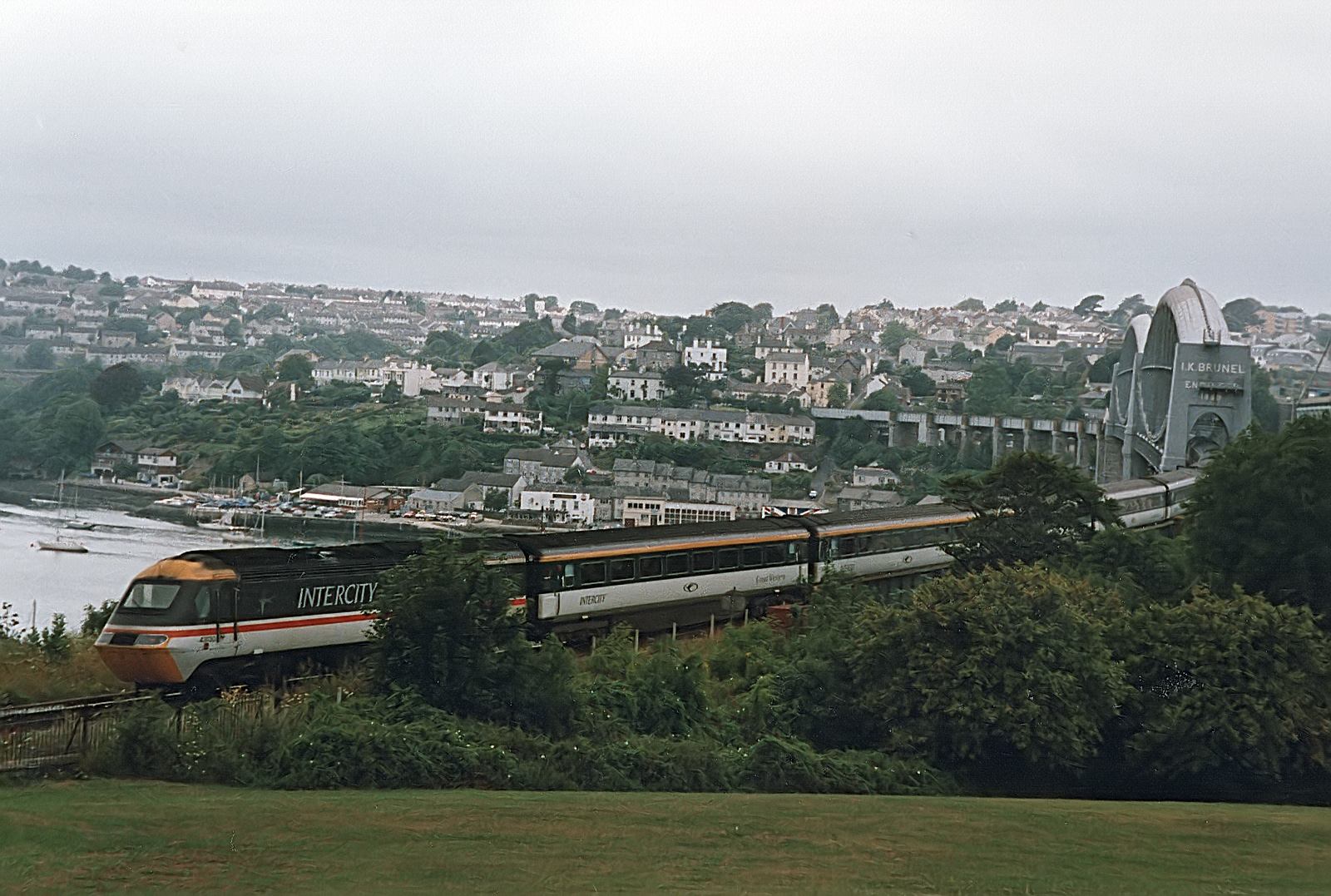 Power car 43130 brings up the rear of a Penzance bound express, about to cross the Tamar river by the Isambard Kingdom Brunel bridge. Typical of this period in the late 90's, the coaches are in the new (at the time) Great Western livery, however the power car has yet to visit the paint shops, remaining in Intercity Swallow livery.